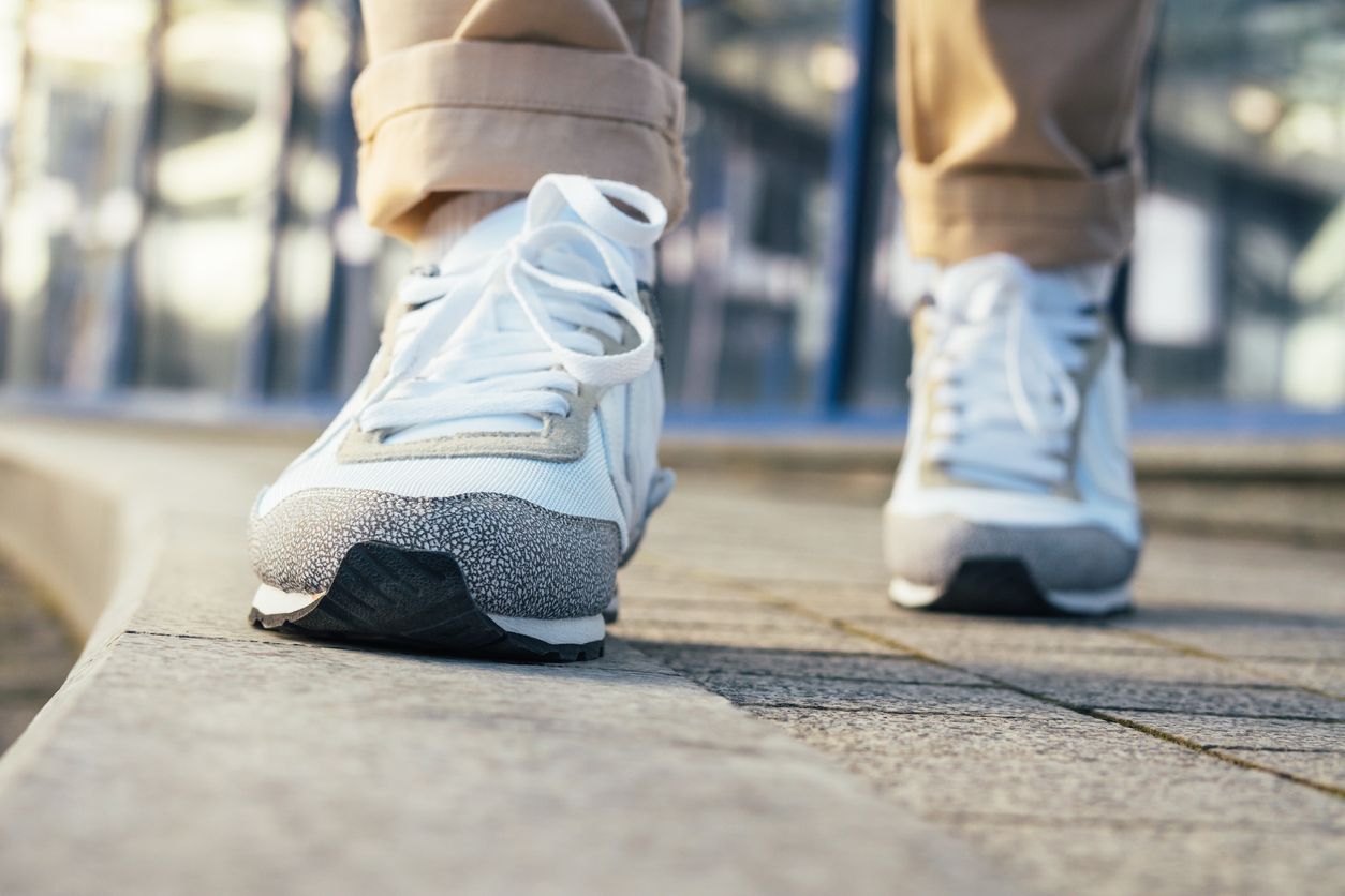 Legs in beige pants and white sneakers are on the sidewalk. Close-up, low angle shooting, shallow depth of field.