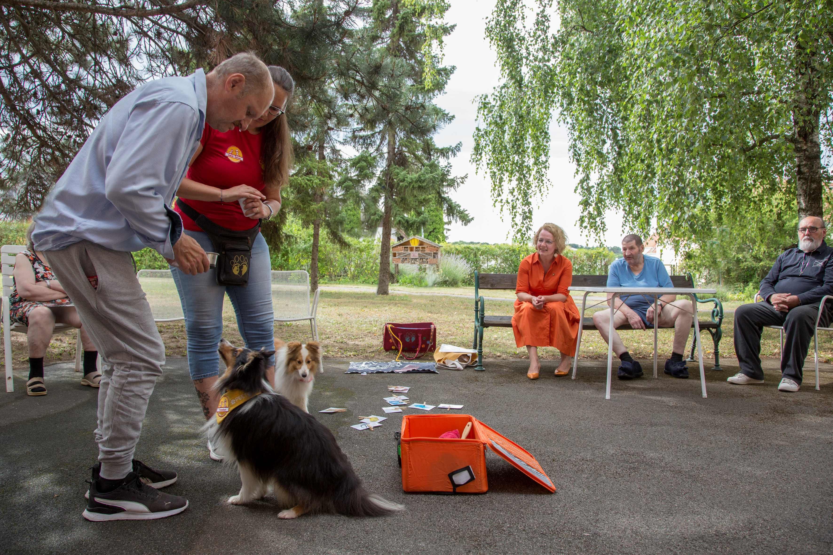 Hundetrainerin Mag. Vera Kainz mit den beiden Vierbeinern und Bewohnerinnen und  Bewohnern bei der Therapie.