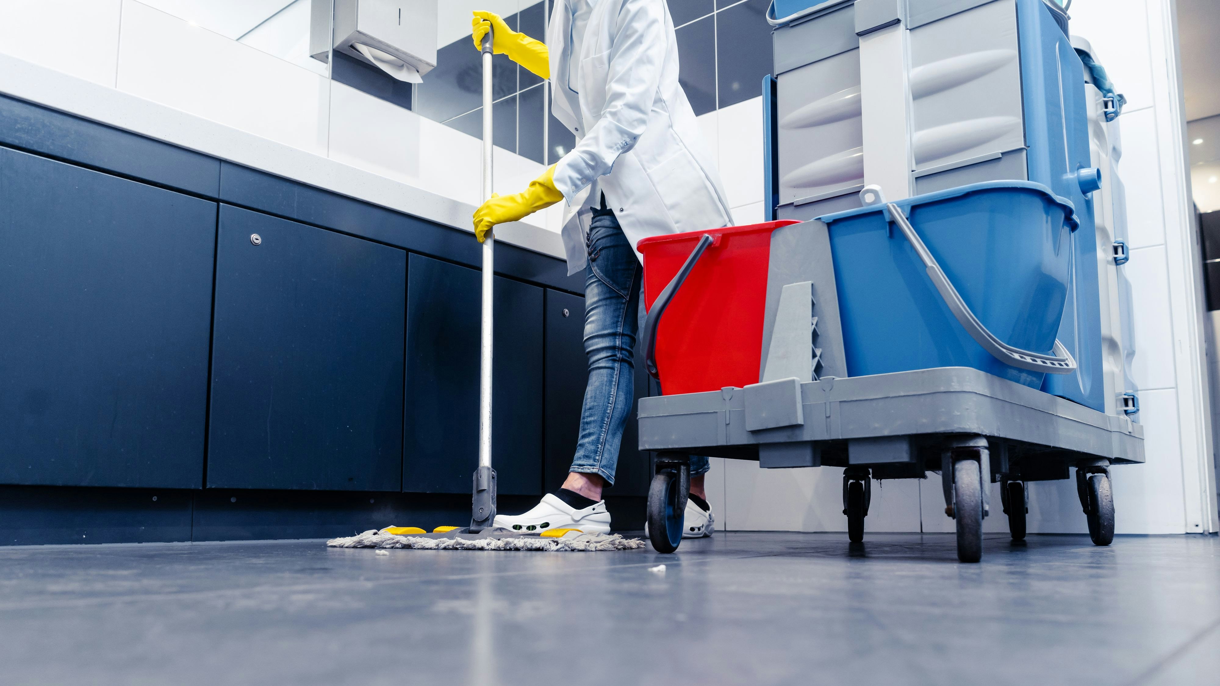 Low shot of cleaning lady mopping the floor in restroom beside her trolley