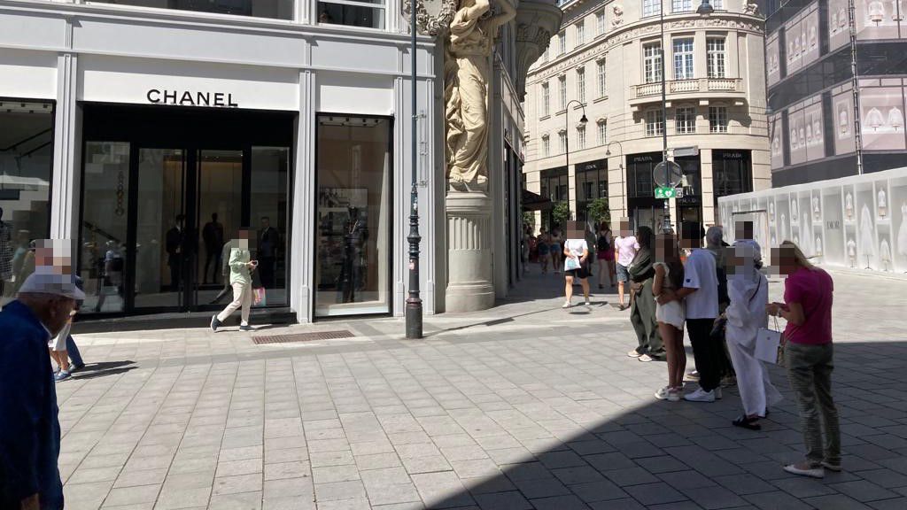 Touristen warten im Schatten auf Einlass in Luxus-Store