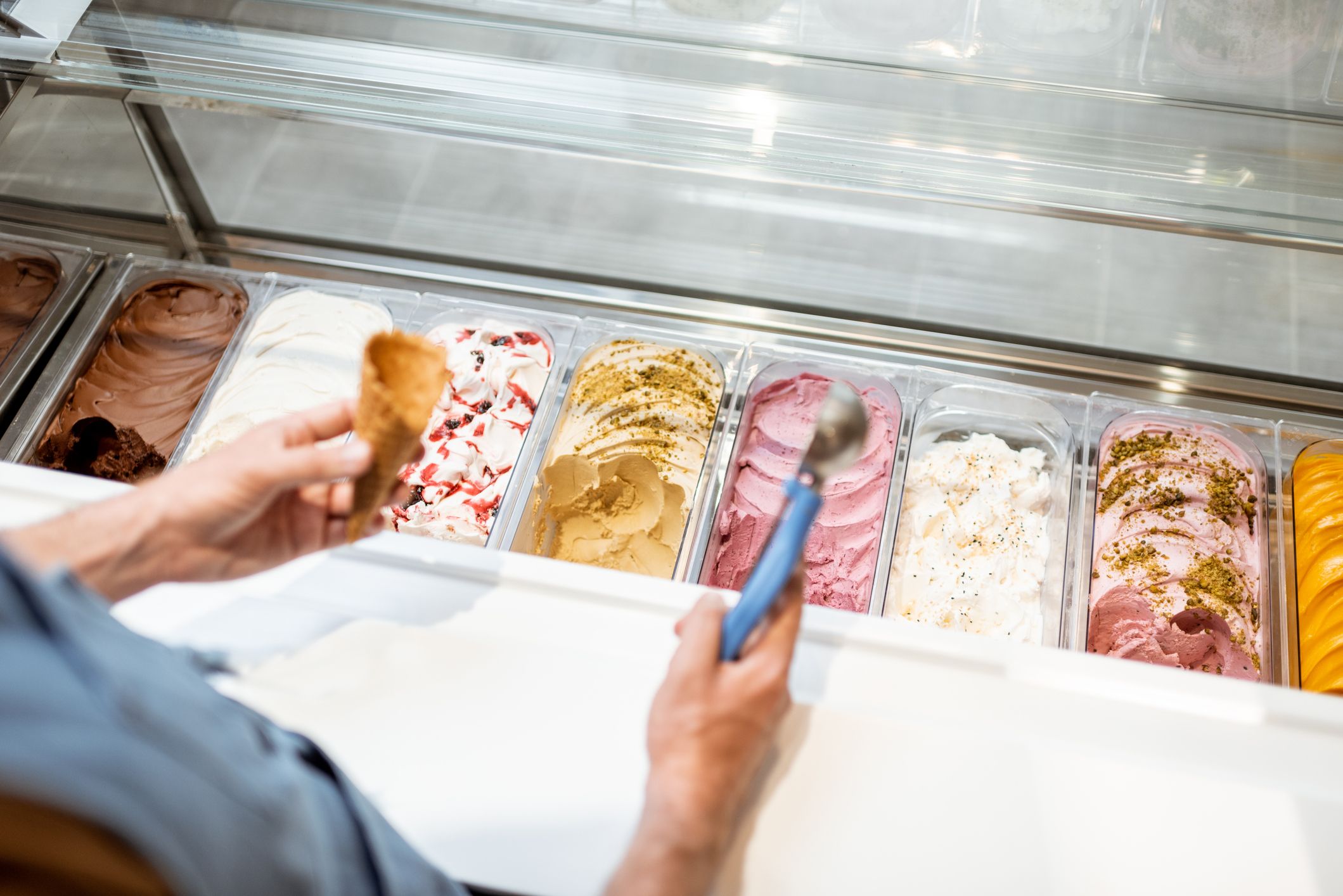 Salesman picking ice cream with a spoon from refrigerator in the store. View from above on a trays full of ice cream with different flavors