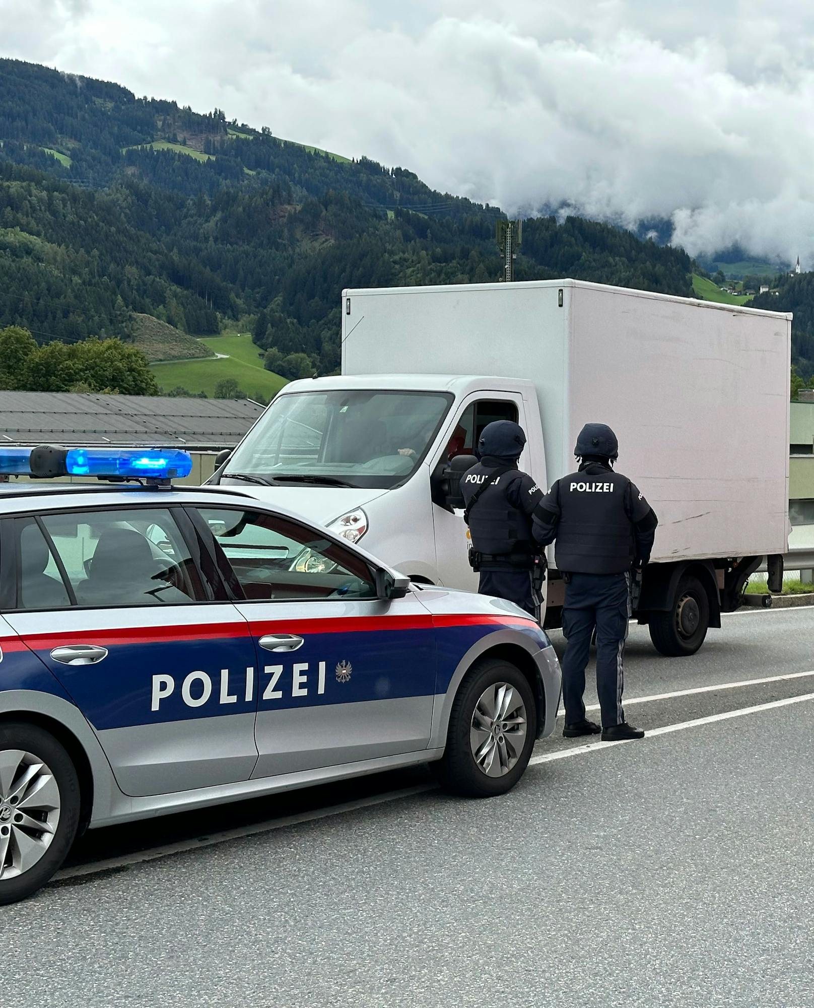 Schwer bewaffnete Polizisten kontrollieren Fahrzeuge in der Umgebung.