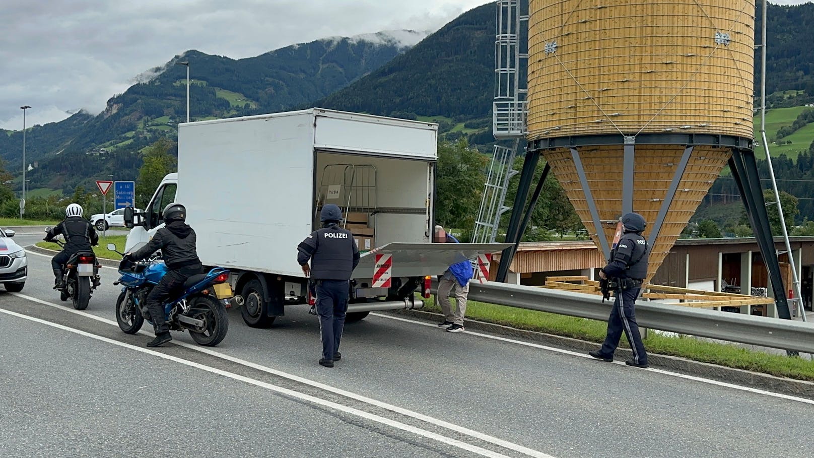 Schwer bewaffnete Polizisten kontrollieren Fahrzeuge in der Umgebung.