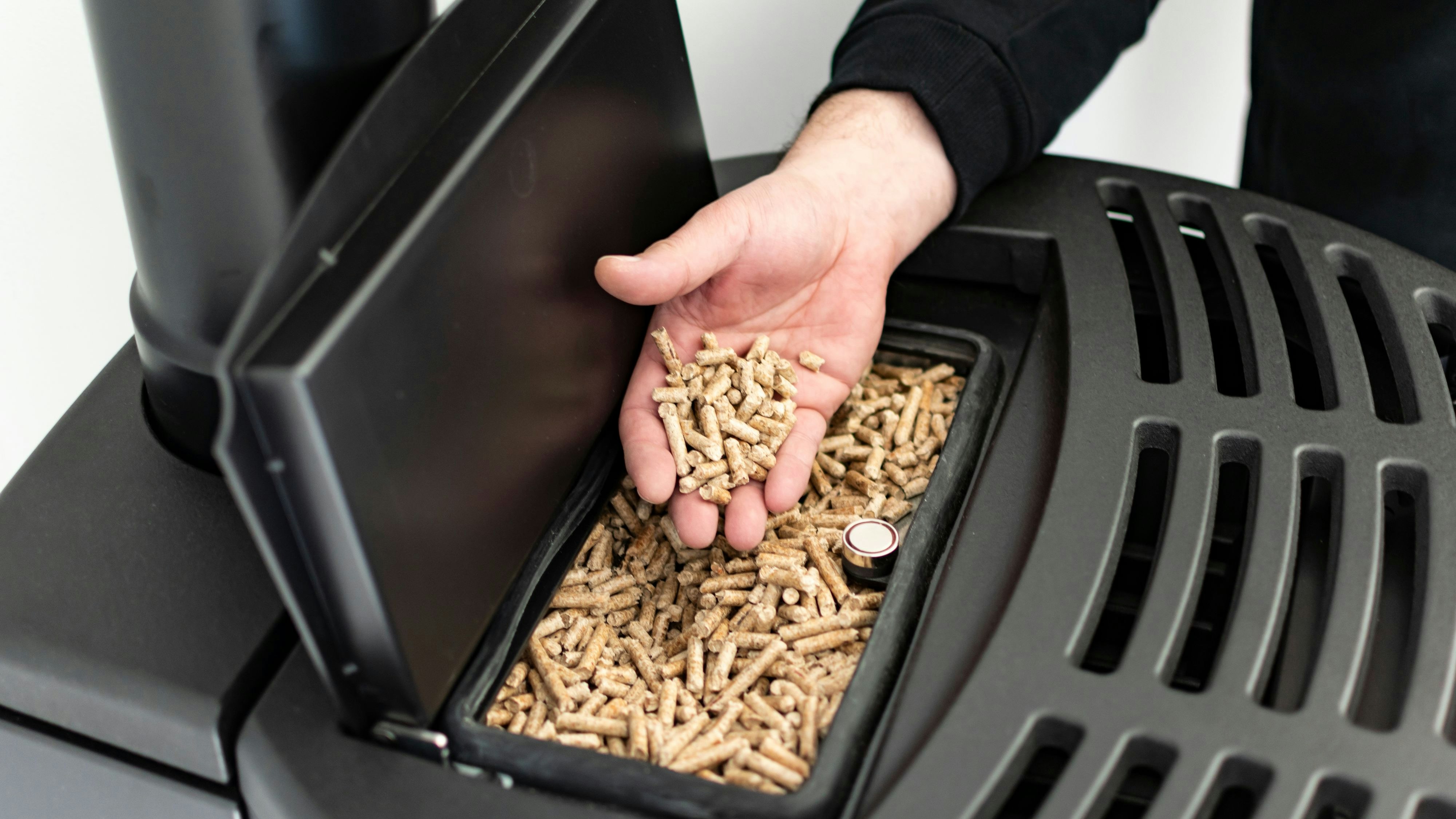 Pellet stove, man holding granules in his hand above a modern black stove