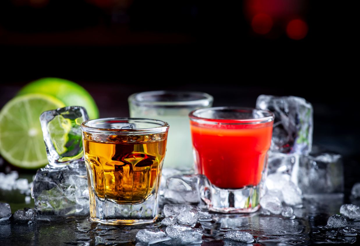 Golden tequila with sangrita and lime juice. Black bar counter background, steel bar tools and bottles