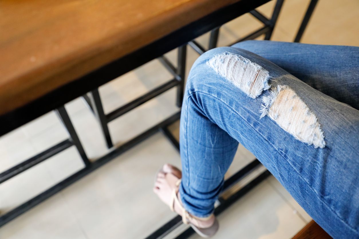Hole and Threads on Denim Jeans. Ripped Destroyed Torn Blue jeans background. Close up blue jean texture. Torn Jeans.