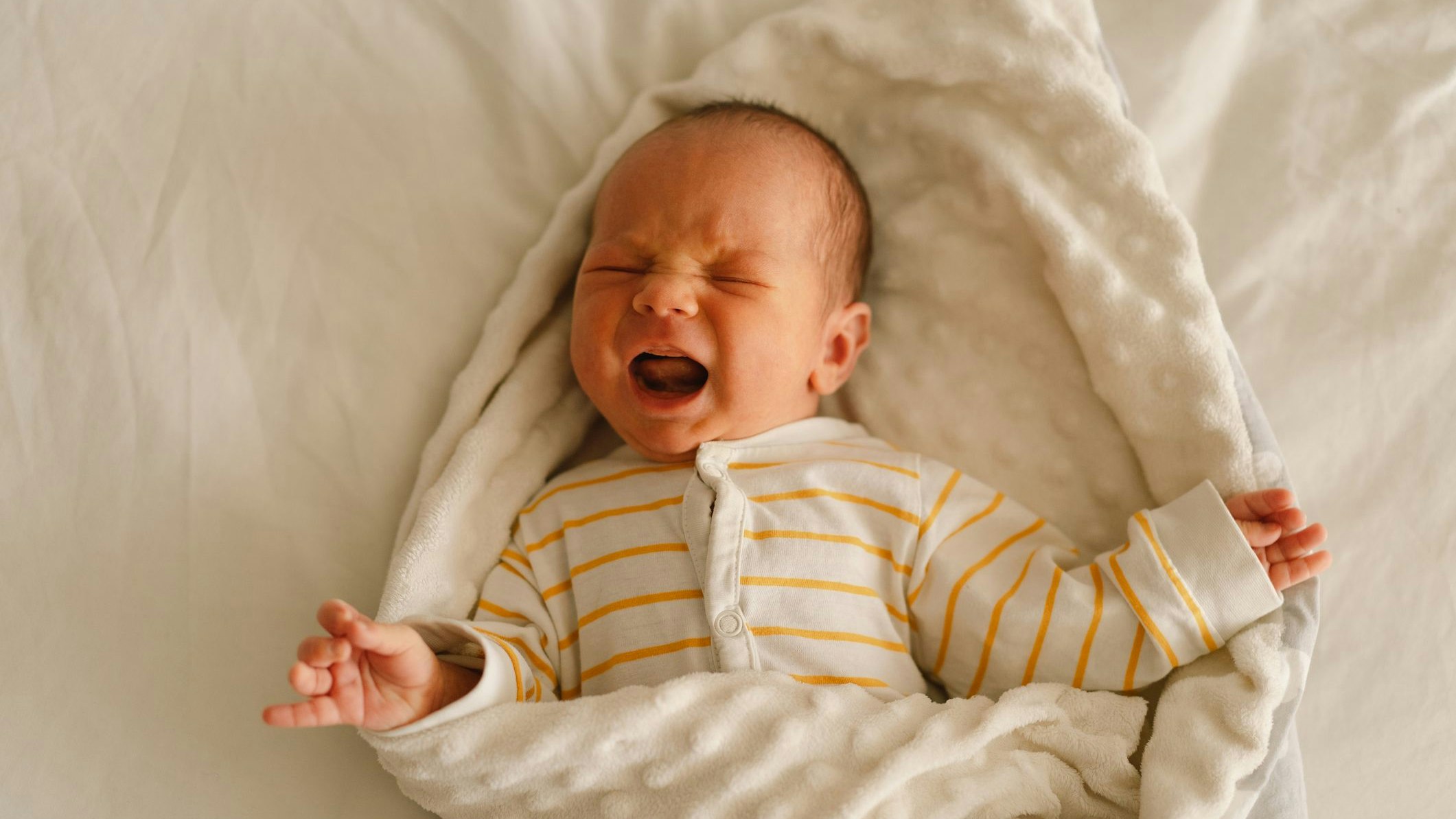 Cute emotional newborn little baby boy cry in crib. Tummy hurts and  emotion. Infant baby.
