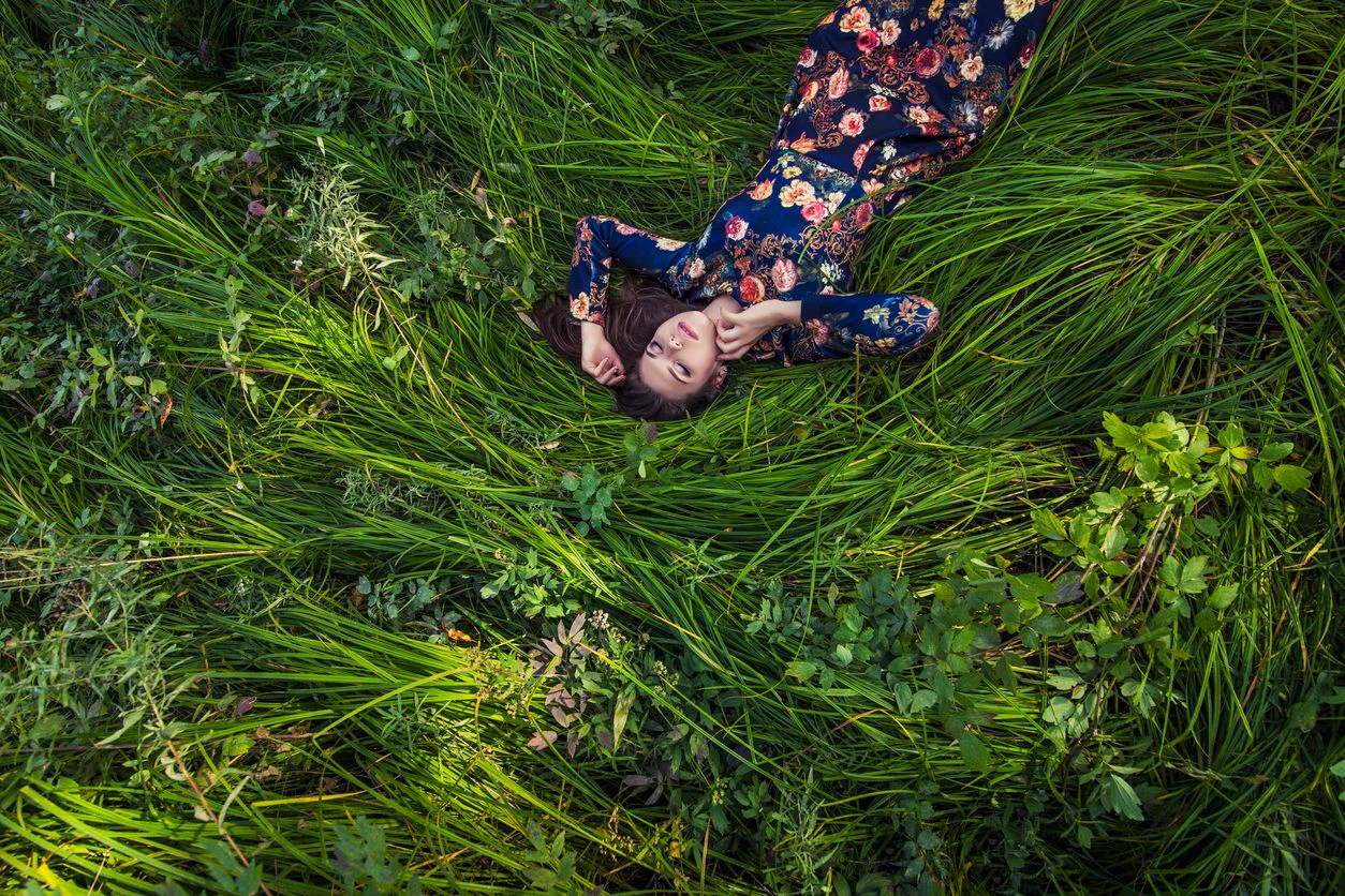Beautiful young woman in dress lying in the grass in nature