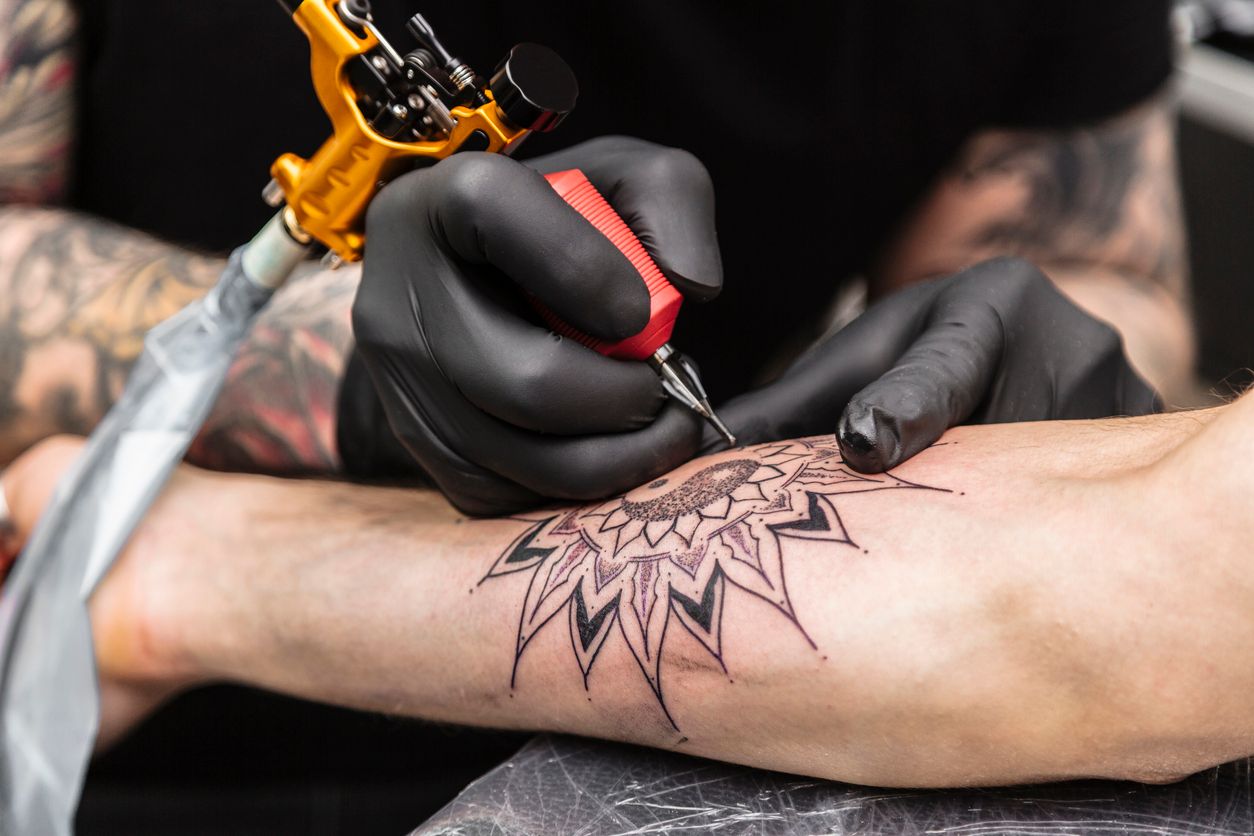Process of creating tattoo in form of black flower. Master does work in sterile gloves