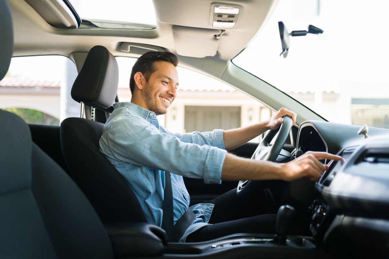 Handsome man in his 30s sitting in the driver's seat and smiling. Taxi driver listening to music on the car and changing the radio station
