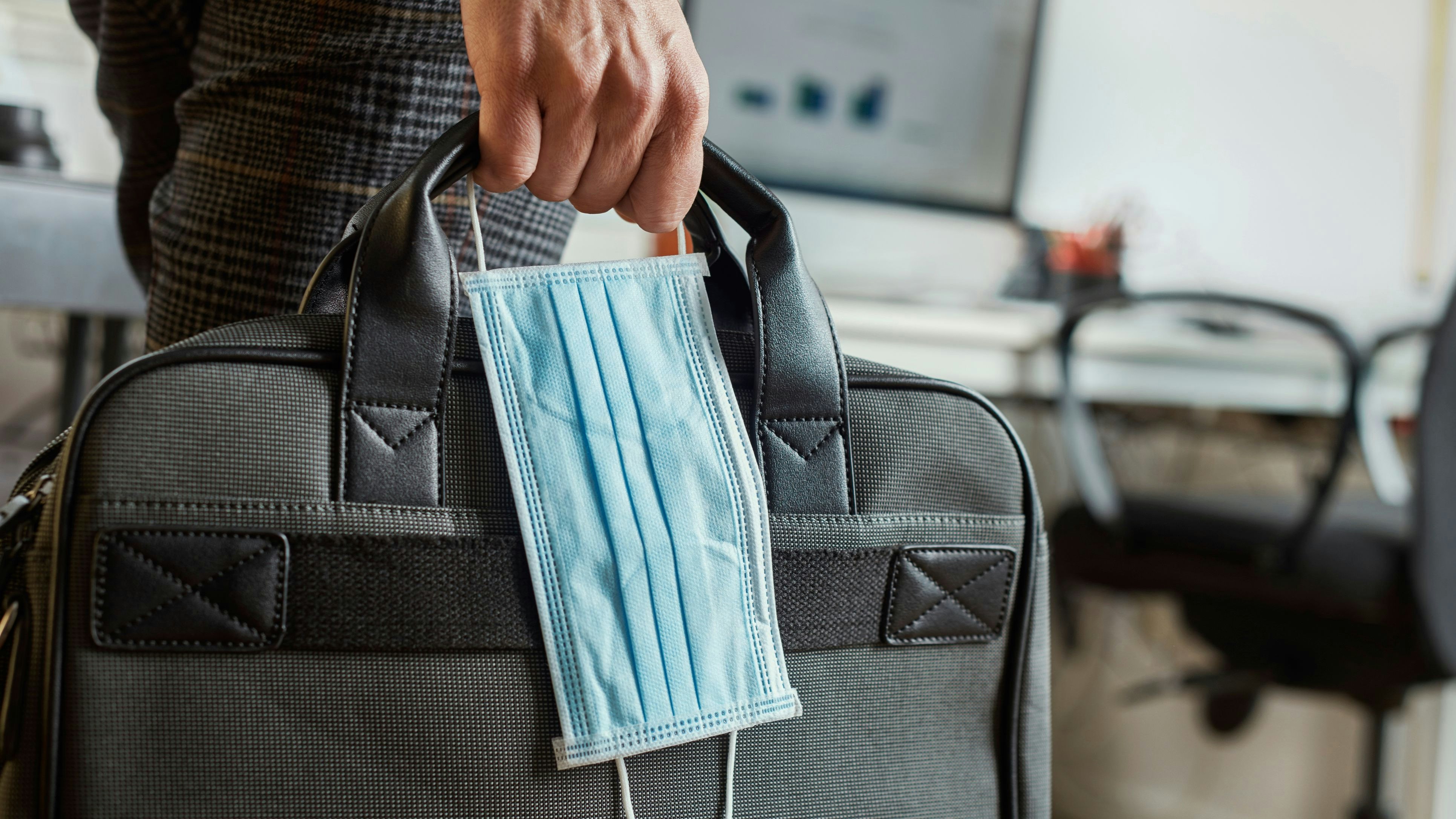 closeup of a young man in an office holding a briefcase and a surgical mask in his hand