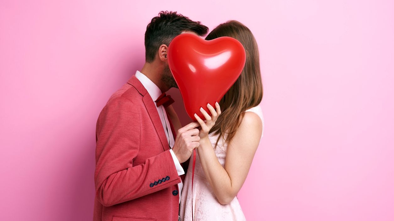 Affectionate couple covering face with balloon and kissing