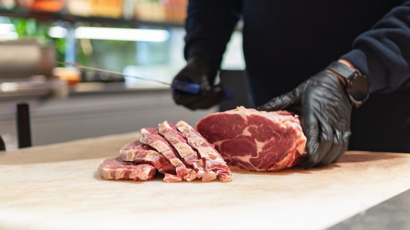 Hands Of A Butcher Cutting Meat On The Cutting Board In Butcher Shop