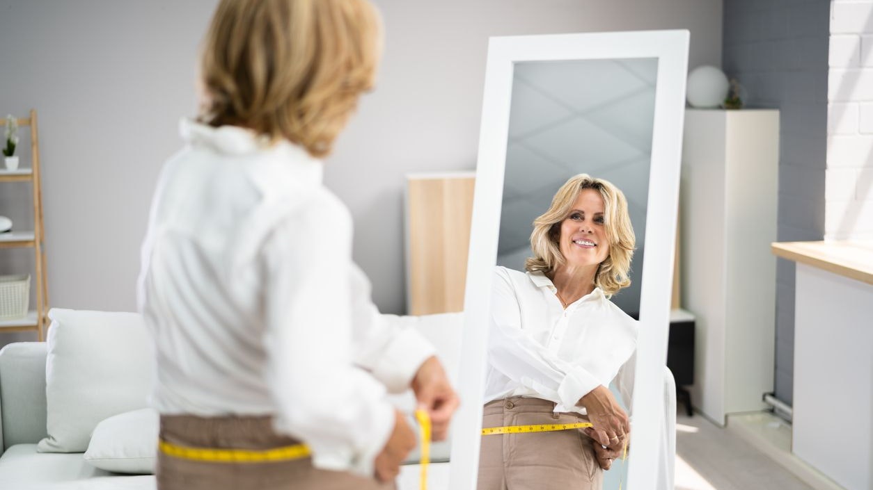 Smiling Slim Woman Looking At Her Reflection In Mirror