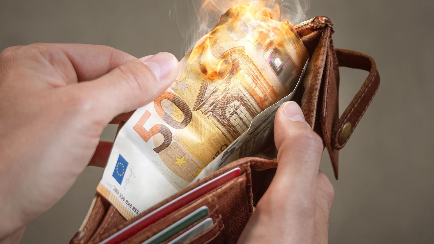 Hands holding a wallet with a burning 50 Euro bill inside.