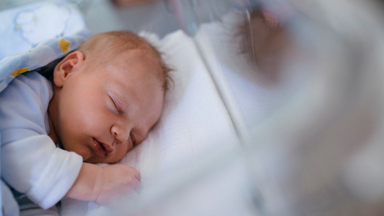 Newborn baby boy lying in a bed. He is sleeping.