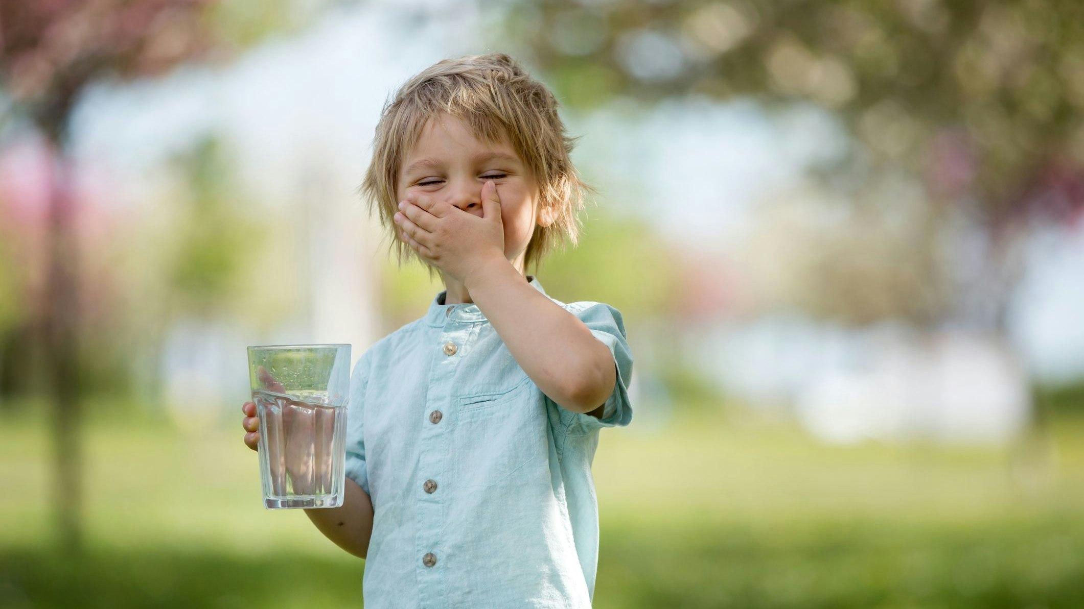 Beautiful blond child, boy, drinking water in the park on a hot summer day