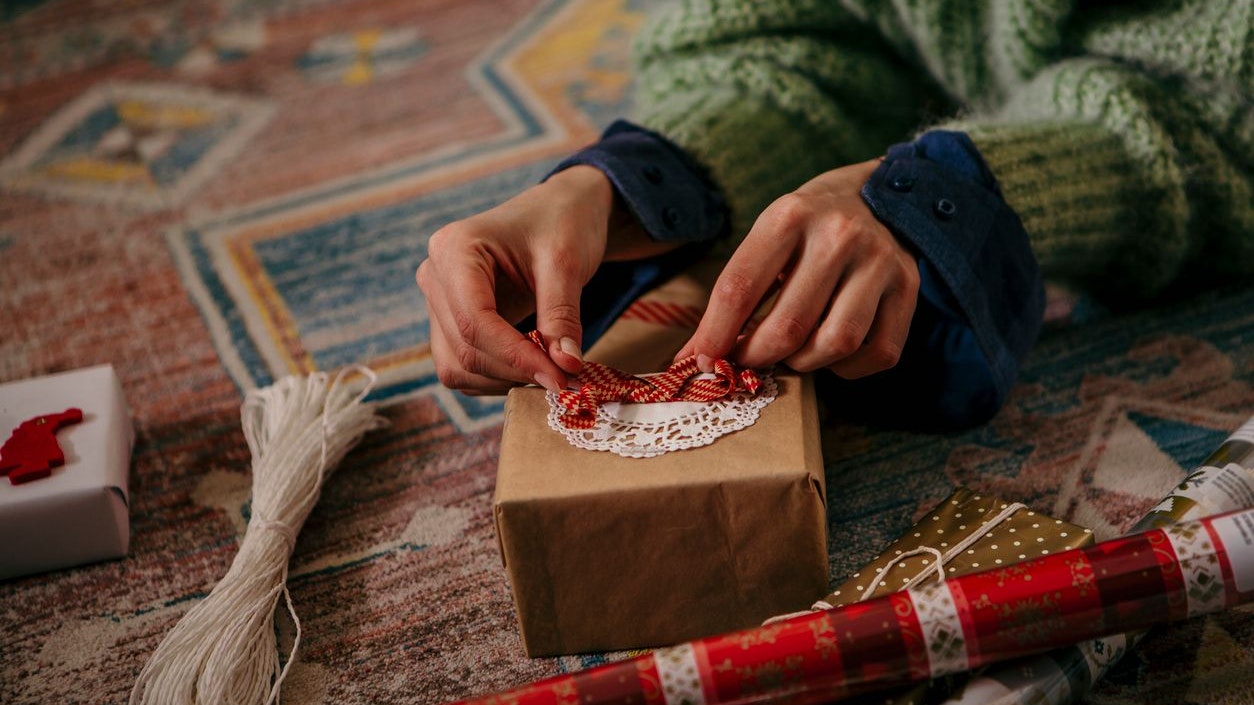 Unrecognizable female hands wrapping a gift while having everything prepared on the floor. A sizers, gift paper, tie and a cute present ready to be wrapped. Just finishing the cute bow. All homemade