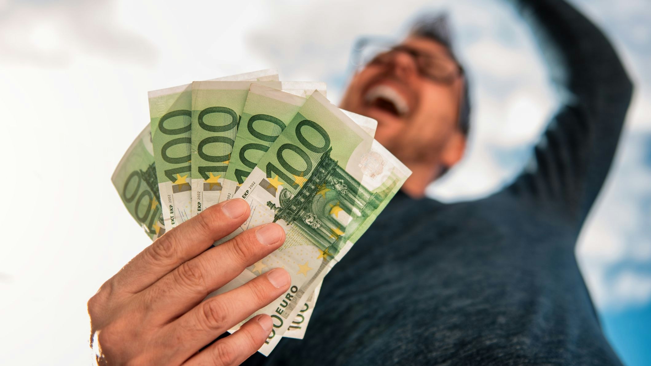 Man with glasses wearing blue shirt. and holding stack of money.