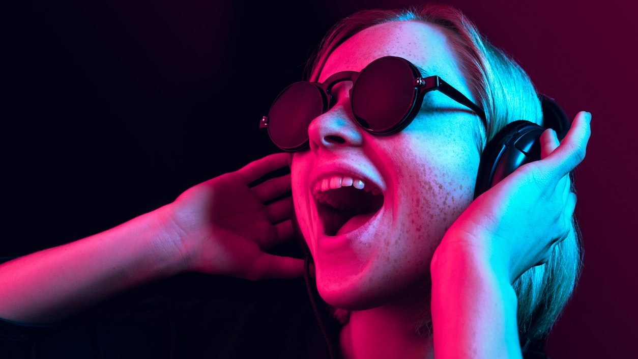 Happy pretty woman with headphones listening to music over red neon background at studio.