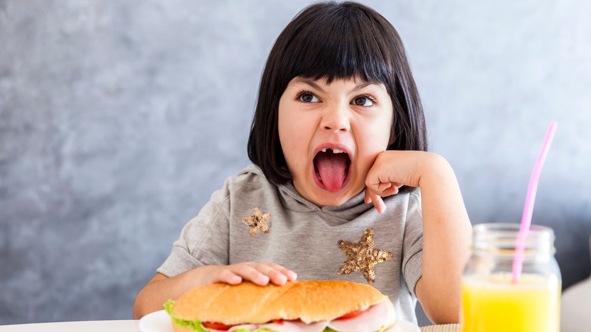 Portrait of little girl having sandwich and juice for breakfast at home