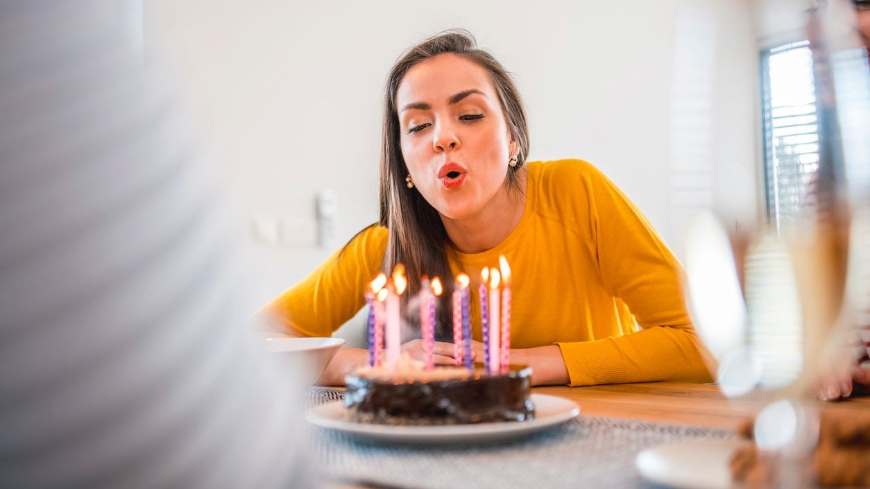 Beautiful young woman blowing candles on cake at dining table. Females are celebrating birthday party of friend. They are at home.