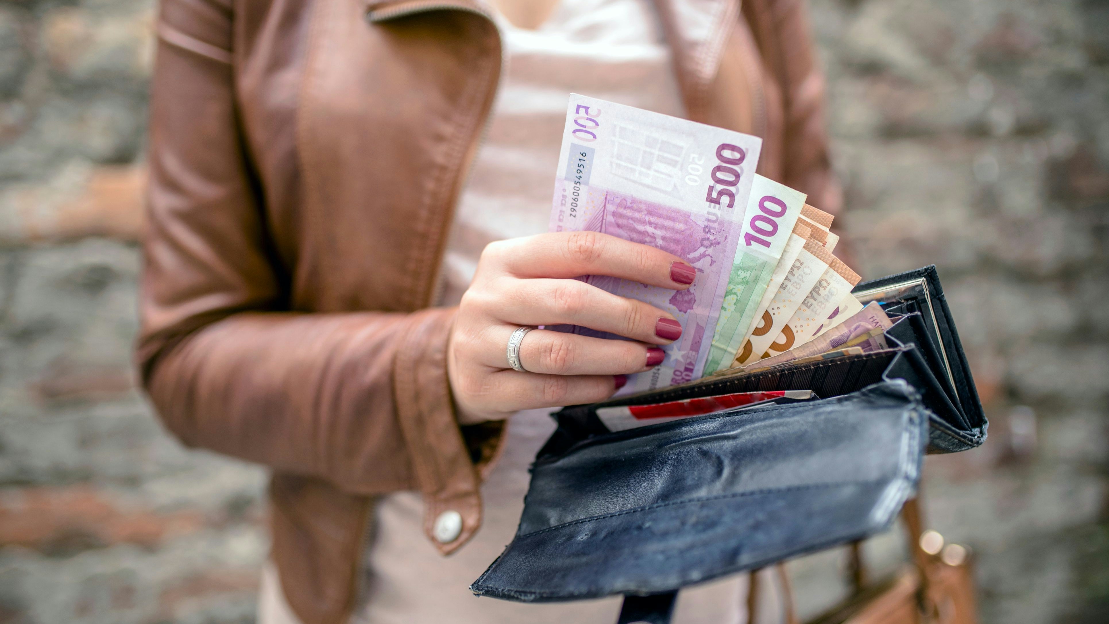 woman taking euro money from black wallet. City girl is taking out money from wallet. Woman hands holding European bank notes