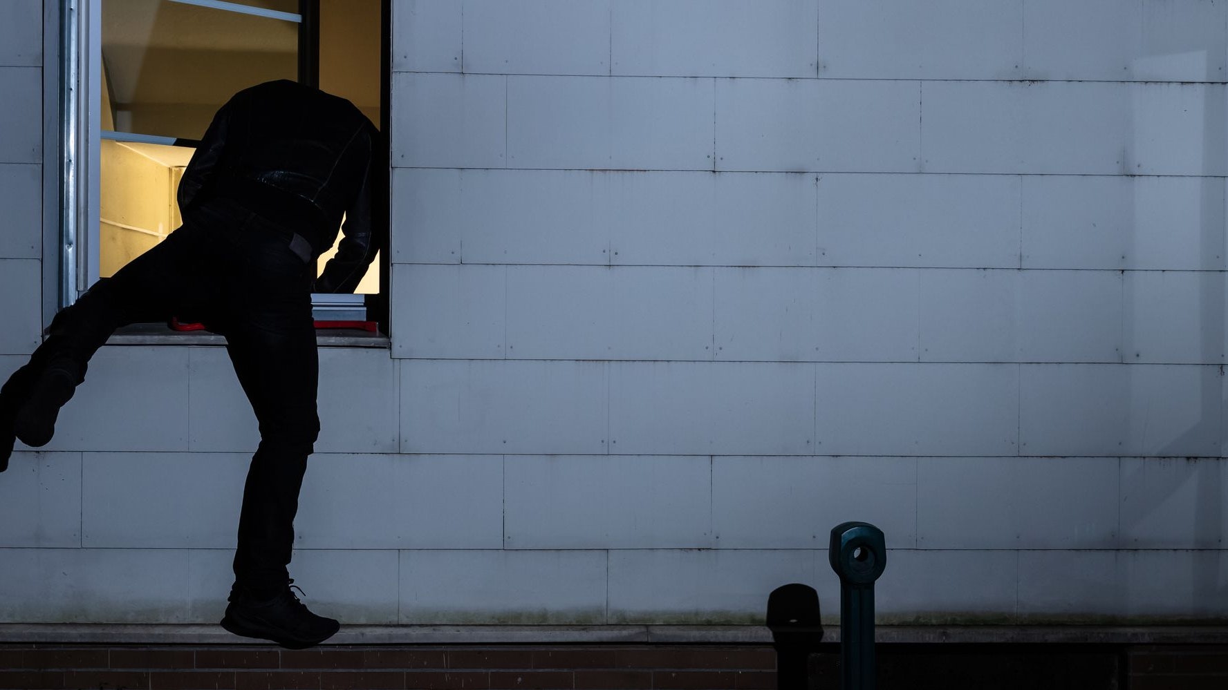 Rear View Of A Burglar Entering In A House Through A Window