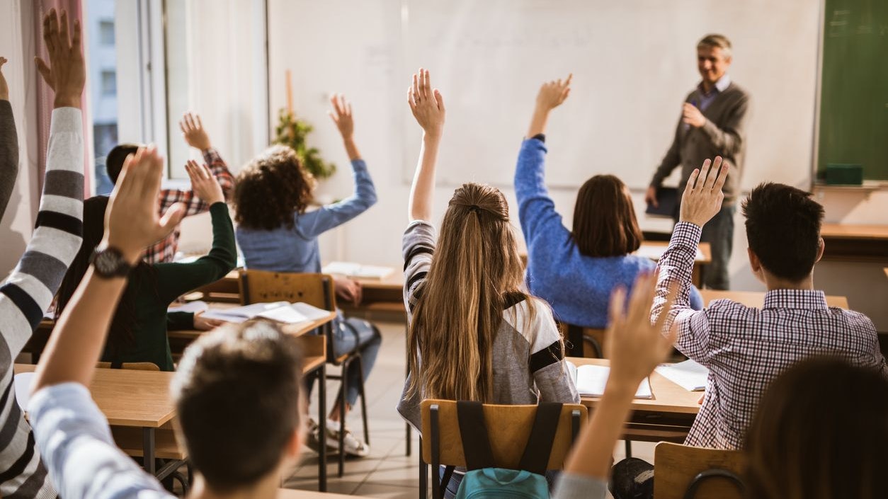 Rear view of large group of students raising their hands to answer the question on a class.