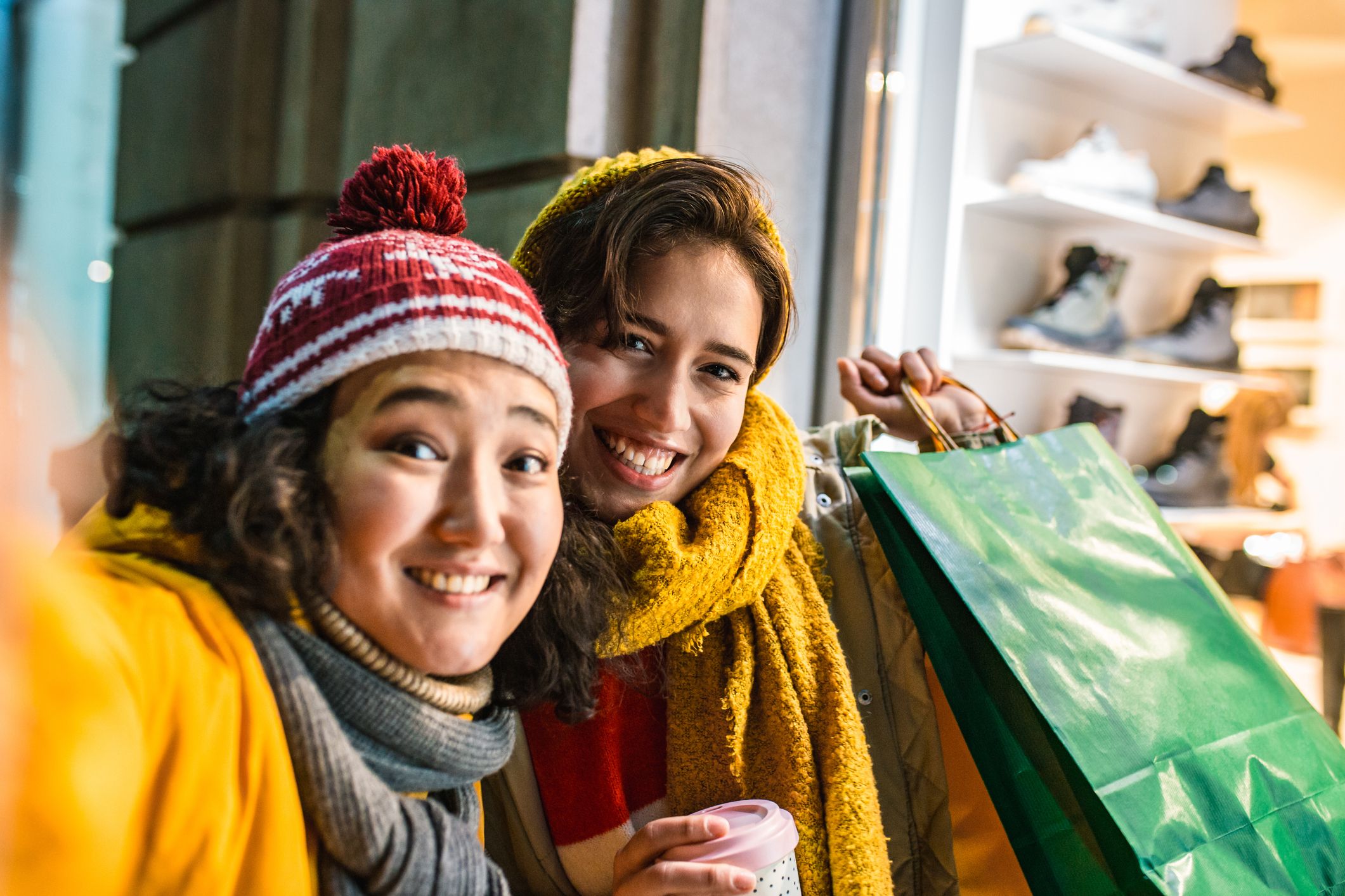 Two female friends are outdoors having fun, they are holding shopping bags and taking selfie on the street
