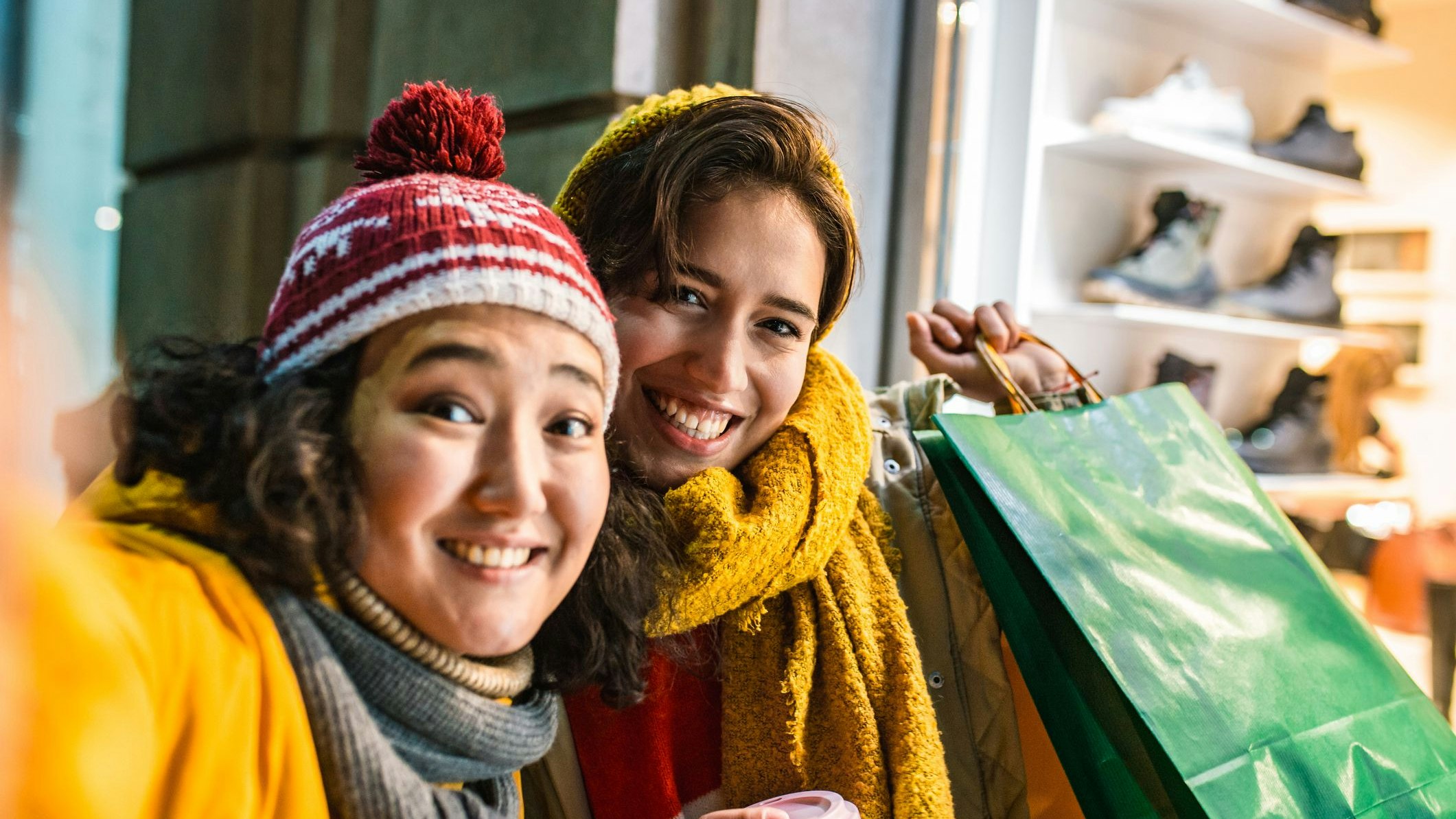 Two female friends are outdoors having fun, they are holding shopping bags and taking selfie on the street