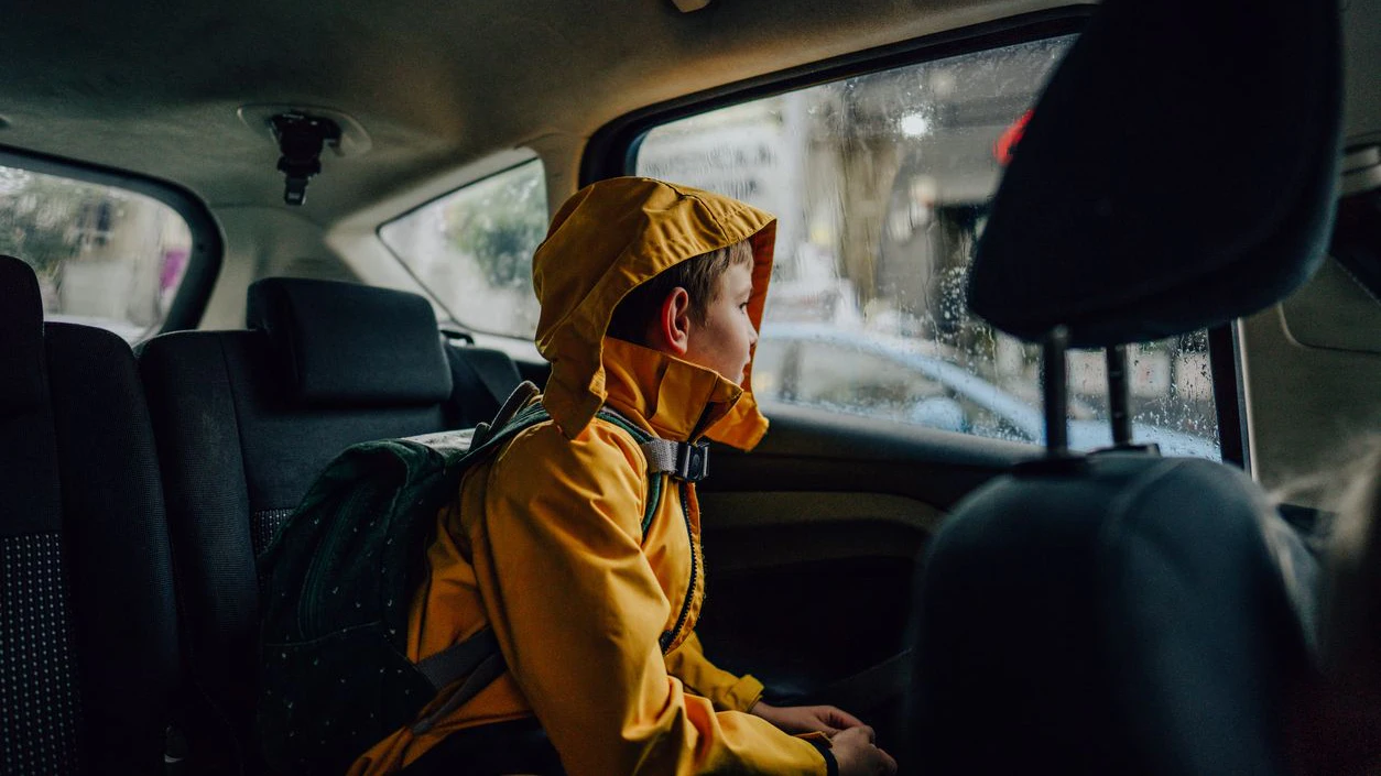 Photo of a young boy, riding in a car on a rainy day