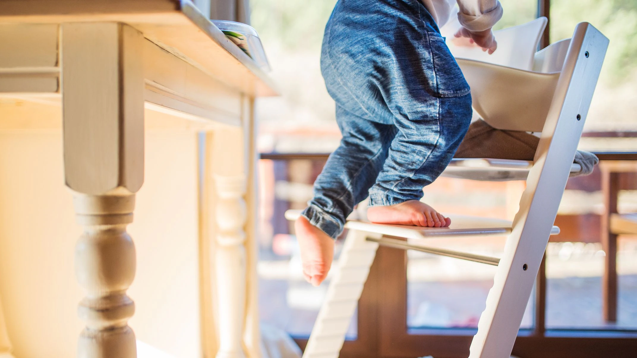 Little toddler boy climbing on wooden highchair at home. Domestic accident. Dangerous situation at home.