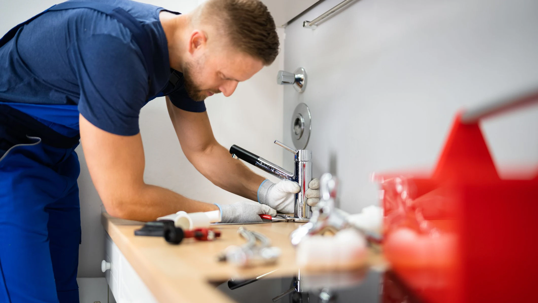 Happy Young Male Plumber Fixing Faucet In Kitchen