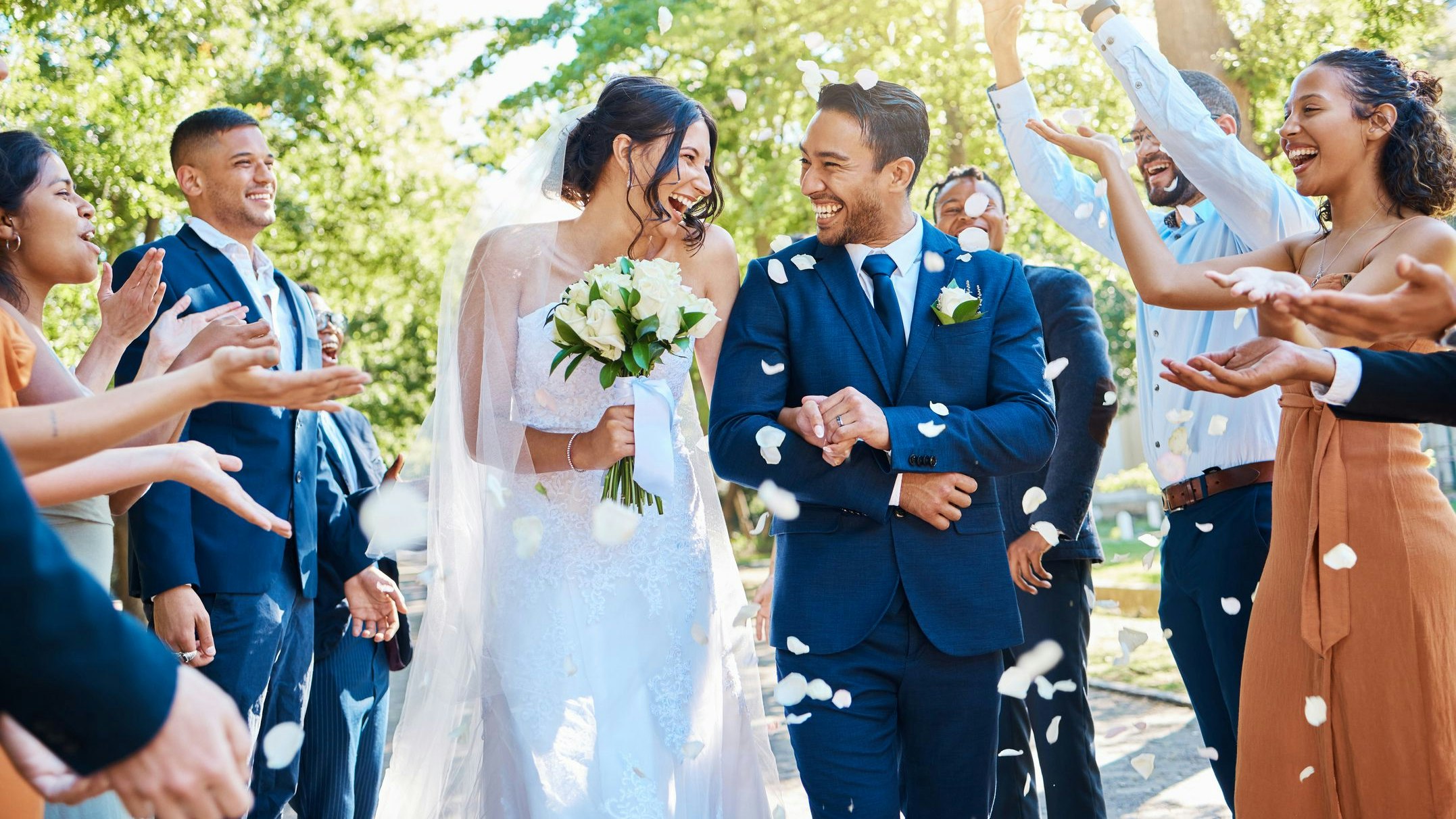 Wedding guests throwing rose petals confetti tradition over bride and groom on their special day. Newlywed couple walking past friends and family