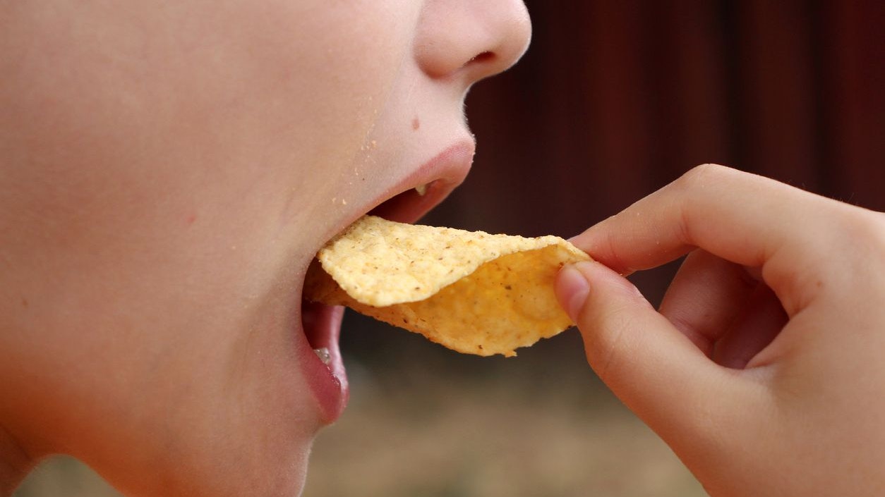 A teenager eats a chips. Close-up photo of a mouth without eyes.