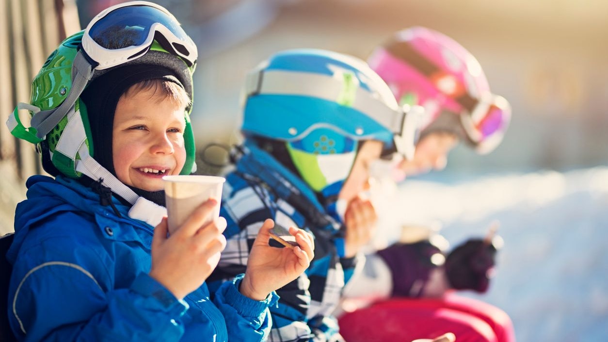 Children skiing on a winter day. Kids are taking a break in skiing and having some hot tea and cookies. 