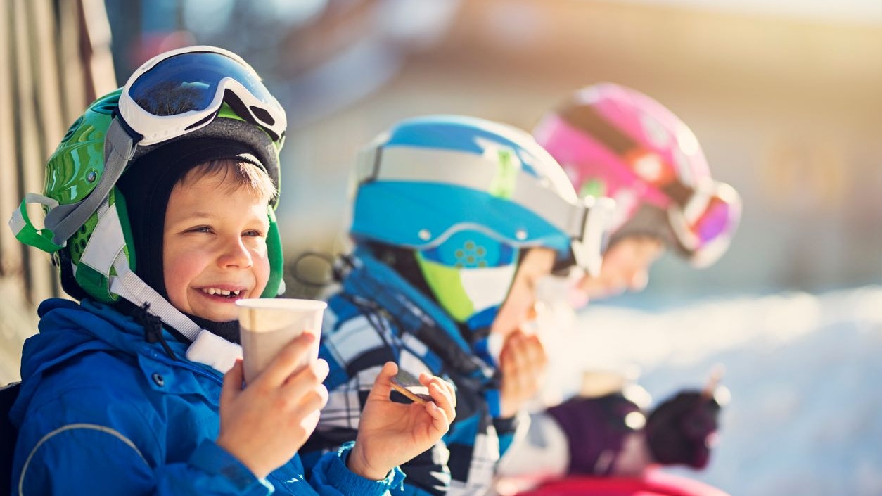 Children skiing on a winter day. Kids are taking a break in skiing and having some hot tea and cookies. 