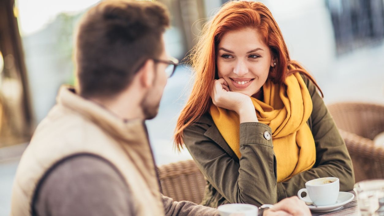 Attractive young couple in love sitting at the cafe table outdoors, drinking coffee