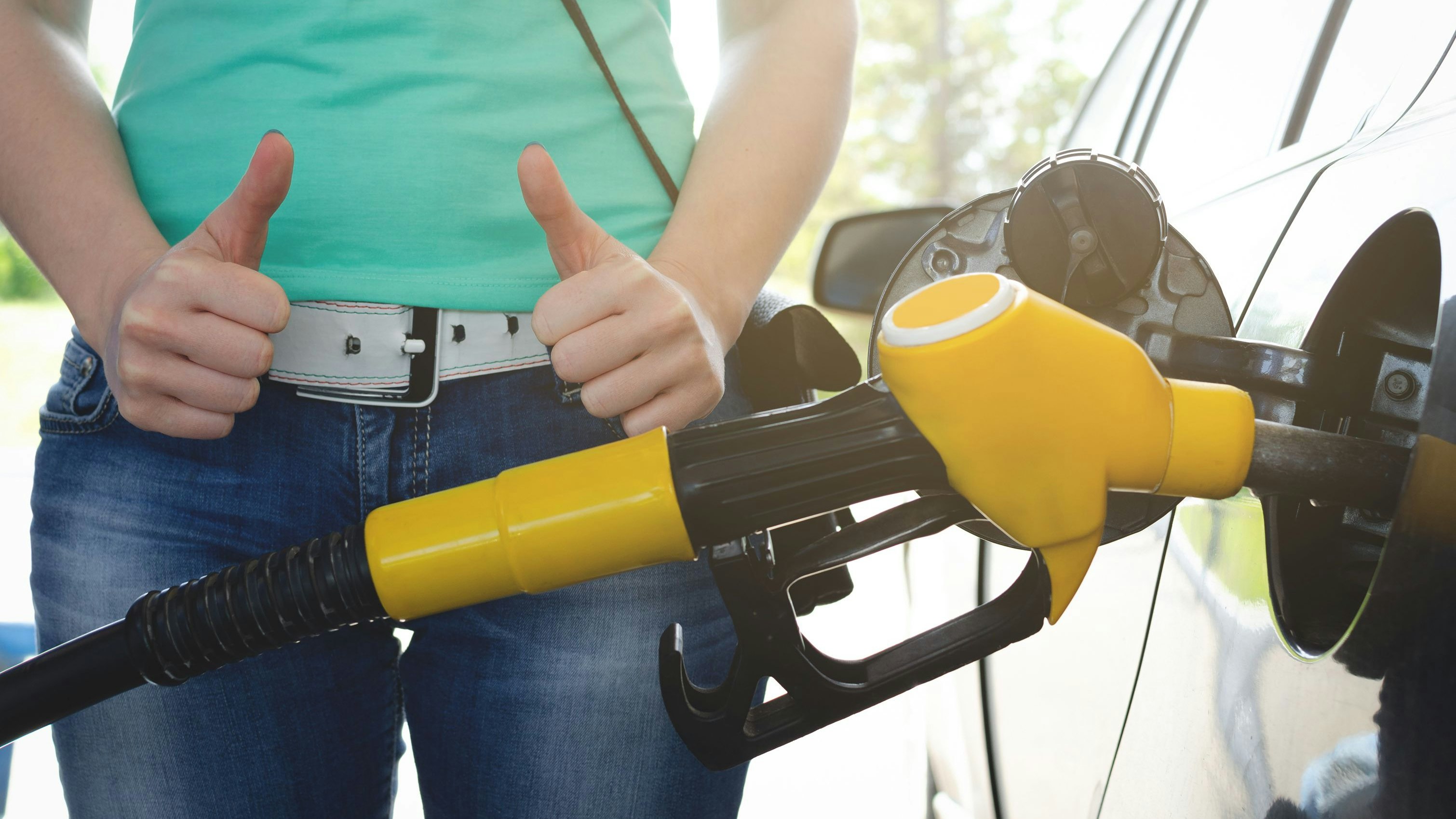 Woman is standing near a fuel nozzle and is showing a thumbs up. High quality fuel concept.