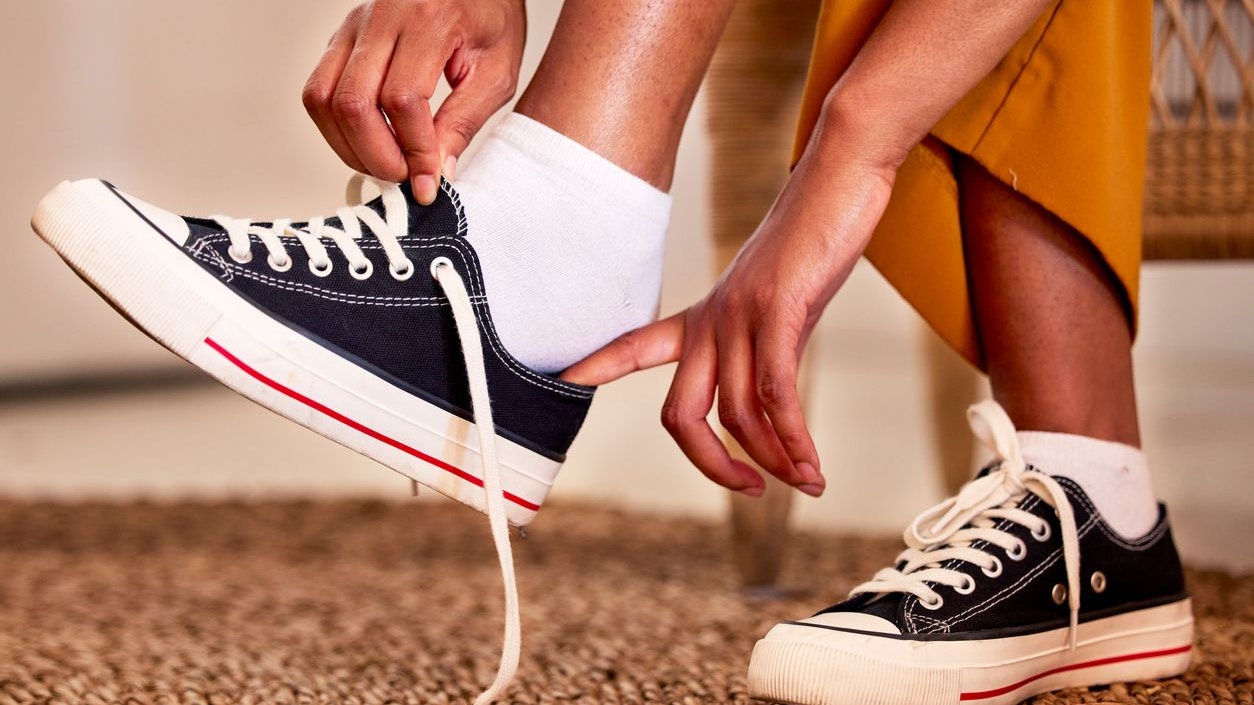 Hands, shoes and lace getting ready for walk, travel or shopping on the carpet floor or mat at home. Hand of person tying laces, fitting or putting on shoe in preparation for walking, journey or trip