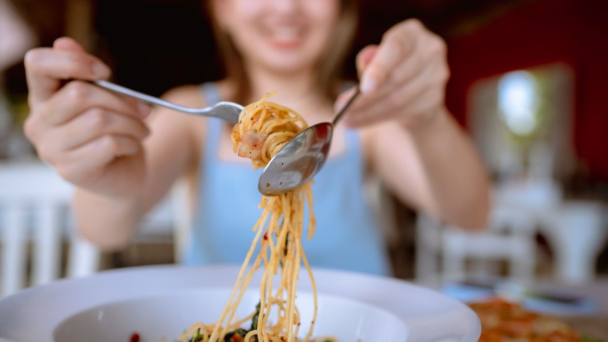 Young Asian woman rolling spaghetti while eating lunch in Italian cafe.
