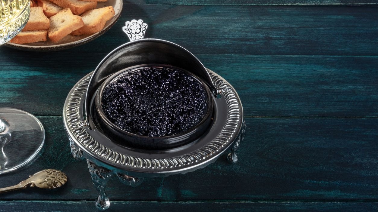 Caviar in a vintage bowl with toasts, with a place for text on a dark blue wooden background