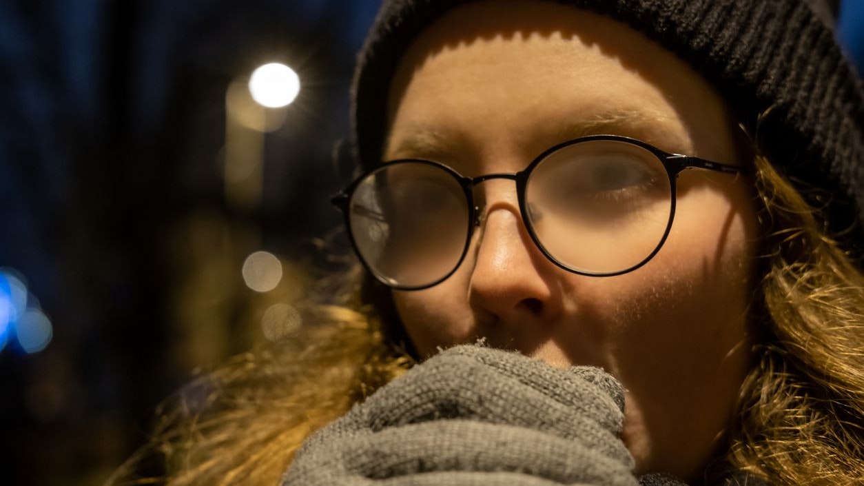 Girl warming her hands with breath, eyeglasses are fogging. It's a cold winter night.