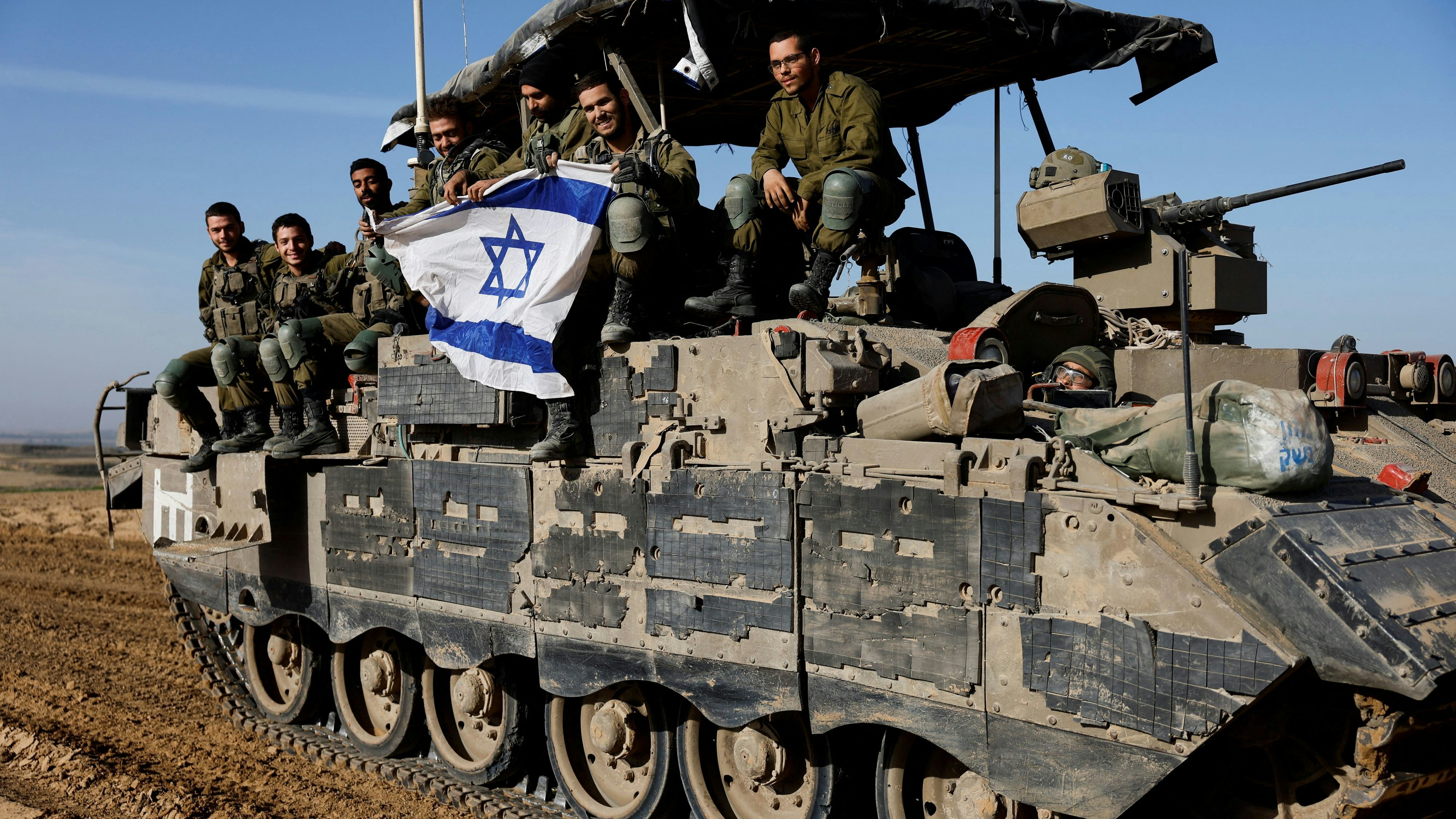 Israeli soldiers hold an Israeli flag atop of a military vehicle, near Israel's border after leaving Gaza, during the temporary truce between the Palestinian Islamist group Hamas and Israel, in Israel, November 24, 2023. REUTERS/Amir Cohen