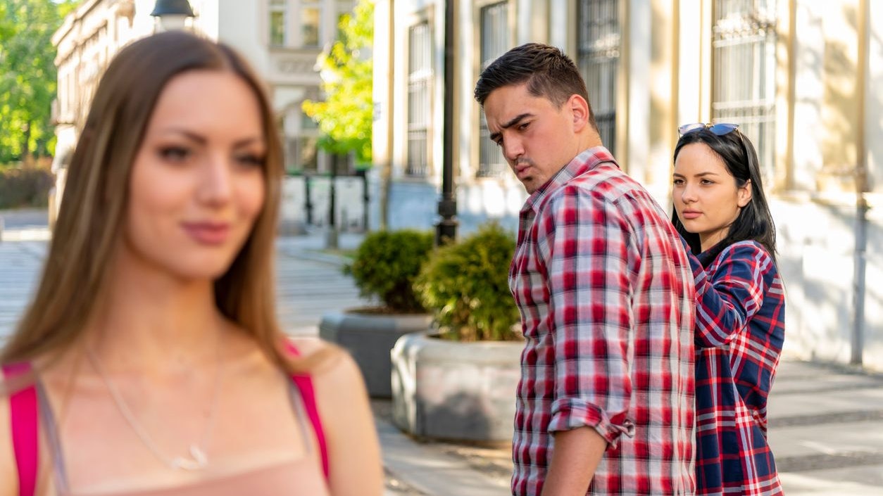 Disloyal man walking with his girlfriend and looking amazed at another seductive girl
