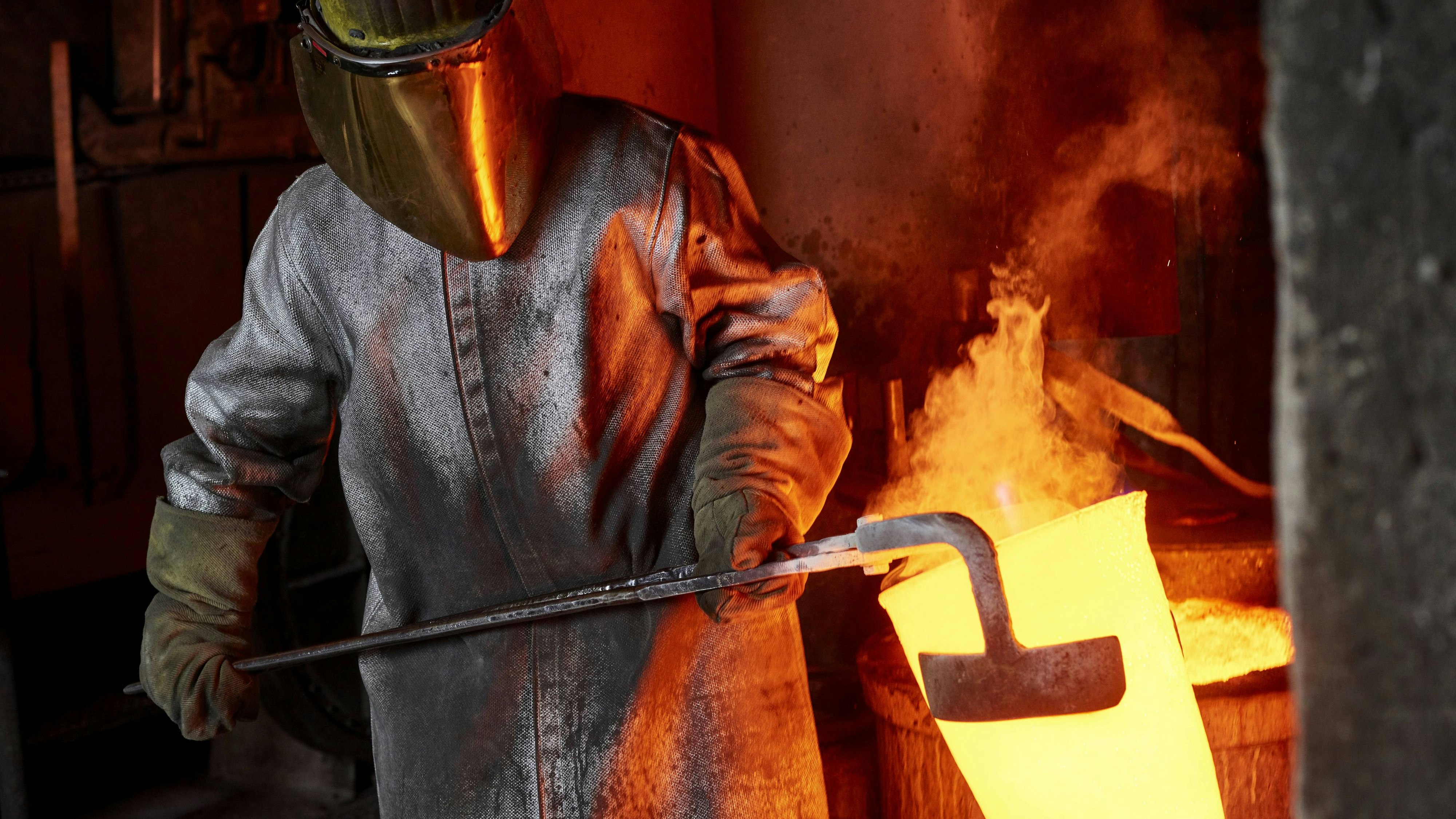 Ein Gießerei-Mitarbeiter mit einem glühenden Schmelztiegel. Symboldbild