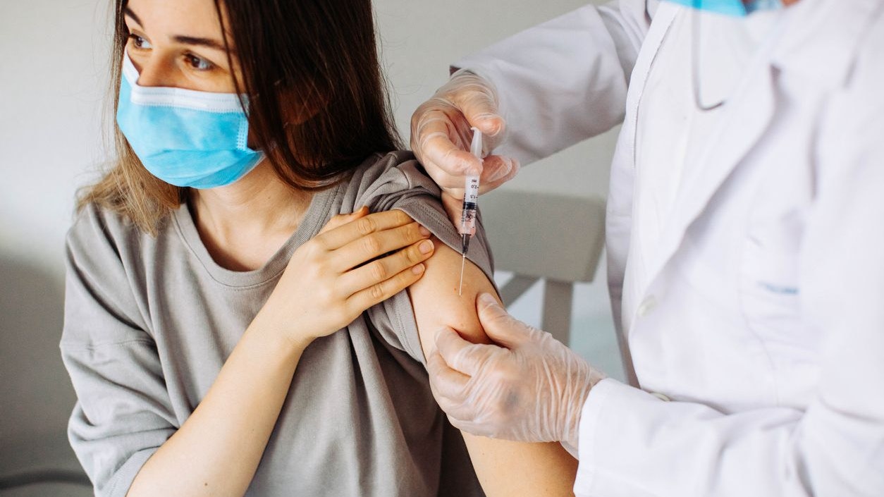 Young woman with face mask getting vaccinated, coronavirus, covid-19 and vaccination concept. Closeup of a nervous woman and her doctor wearing face masks and getting a vaccine shot in a doctor's office