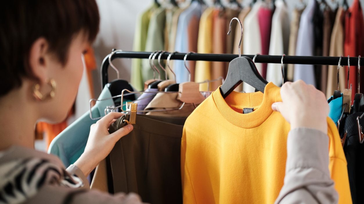 Rear view of young woman looking at clothes on rack in her hands and choosing a new style for herself in the clothes store