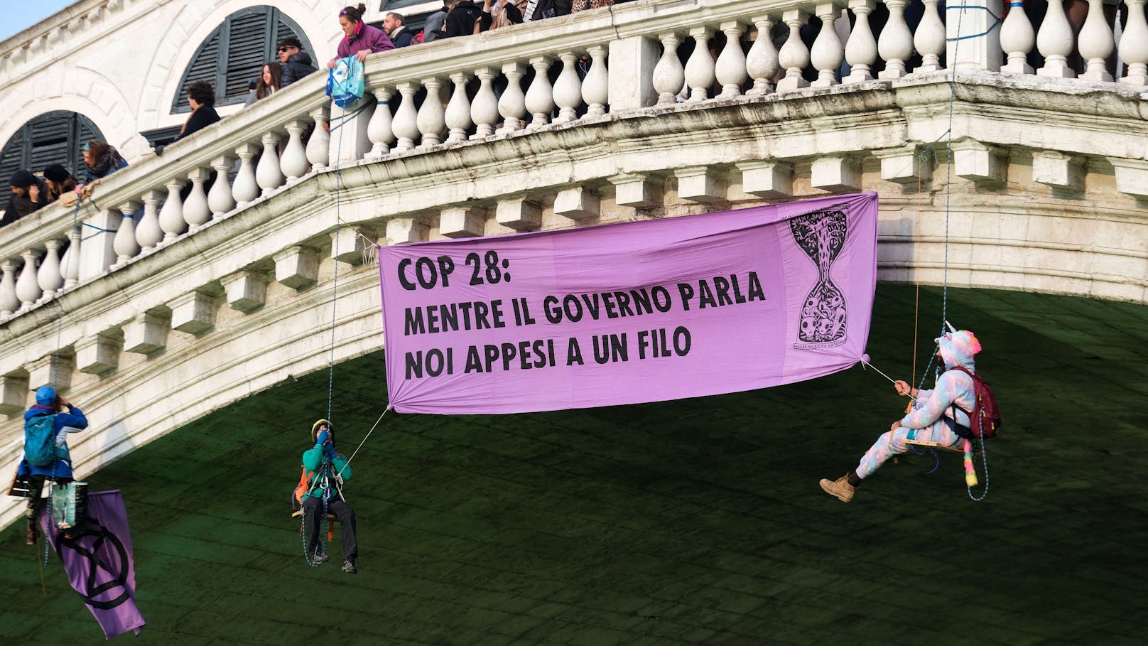 Über dem Kanal hingen drei Aktivisten mit einem Plakat mit dem Schriftzug "COP28: Während die Regierung redet, hängen wir am seidenen Faden".